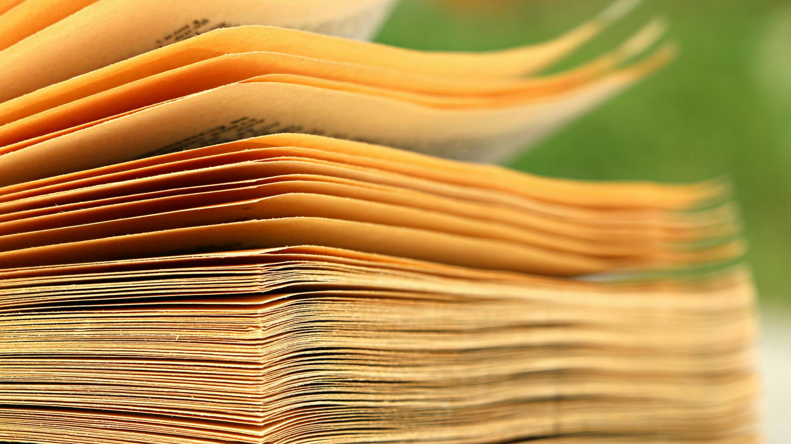 Macro shot of aged book pages with a blurred green background, highlighting texture and detail.
