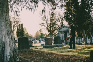 A person stands in a peaceful cemetery holding flowers in remembrance.